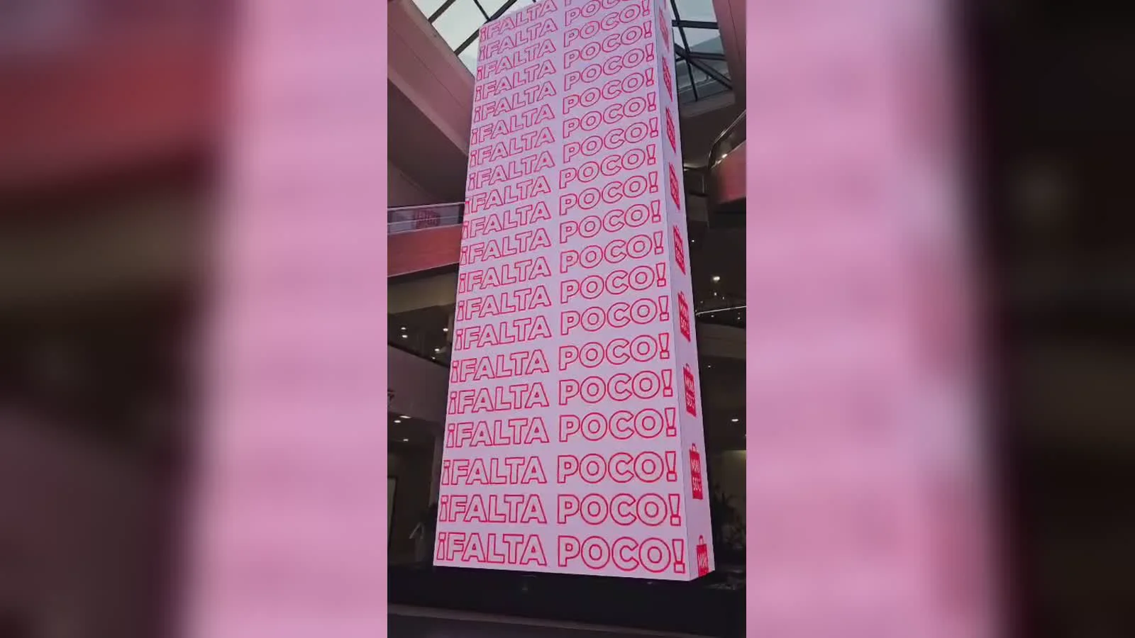 Pantalla LED vertical de MINISO dentro de Unicenter, con la frase ¡Falta poco! repetida en letras rojas sobre fondo rosado, vista desde la planta del shopping