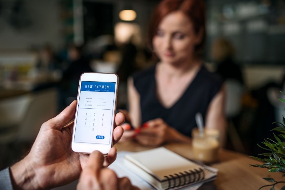  Person holding a phone that says “new payment” on the screen next to a woman. 