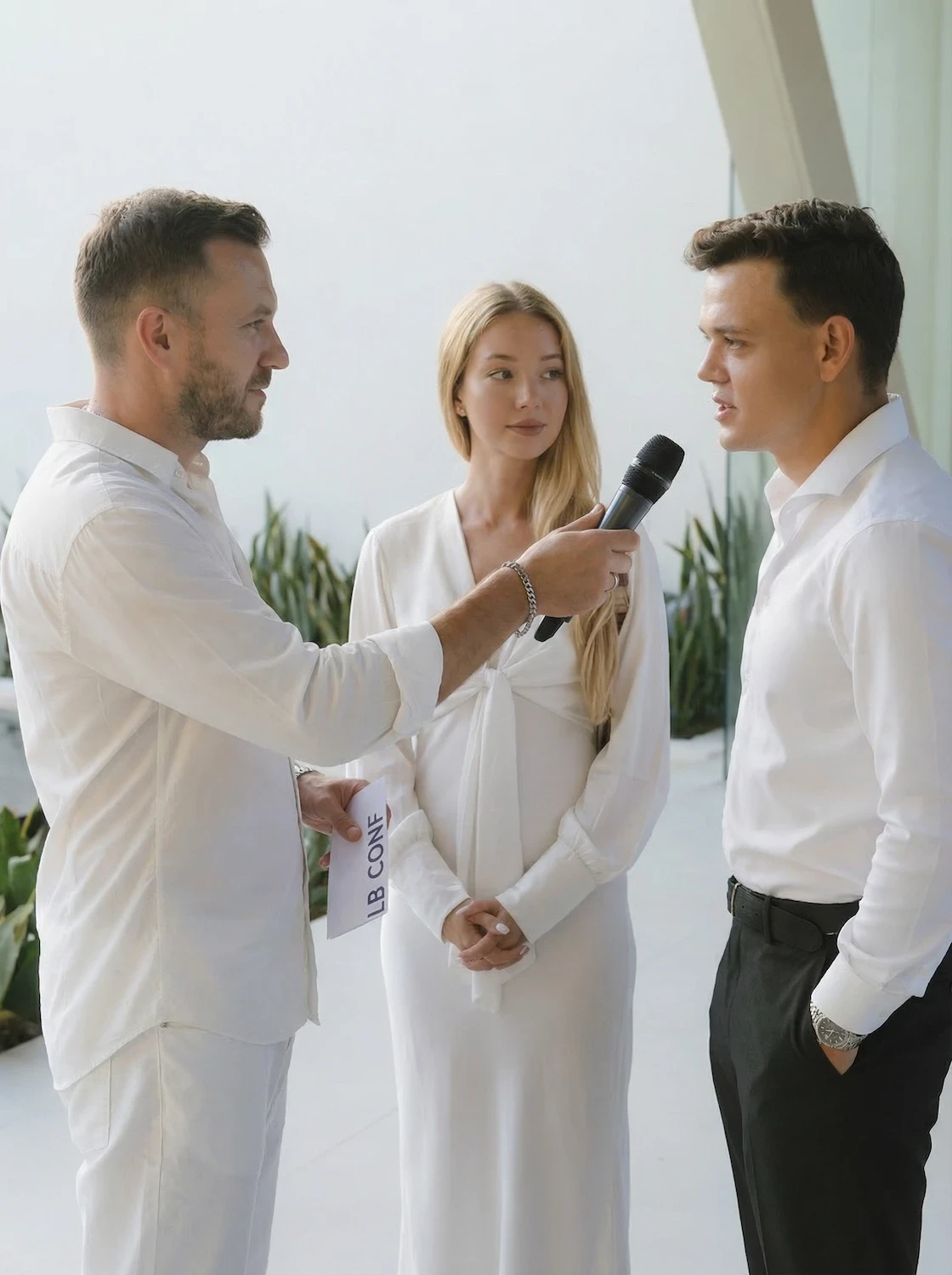 Man with a beard in a dark button-up shirt, smiling while writing in a notebook.