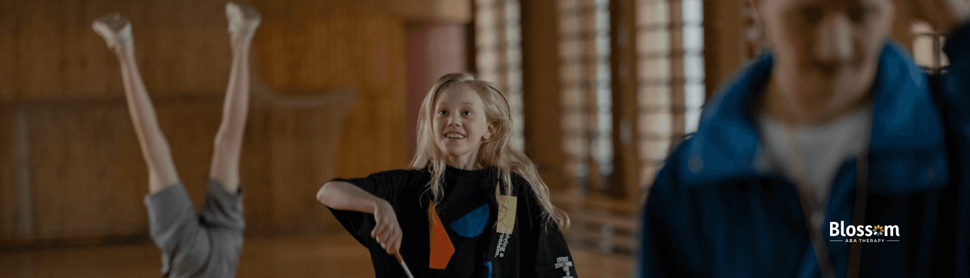 An autistic girl smiling while twirling a gymnastics ribbon during a practice at a school gym in TN.