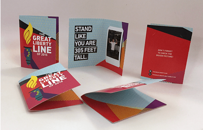 A photo of a colored brochure design. On it there is the lamp of liberty drawn with text: The Great Liberty Line. Stand Like You Are 305 FT tall.