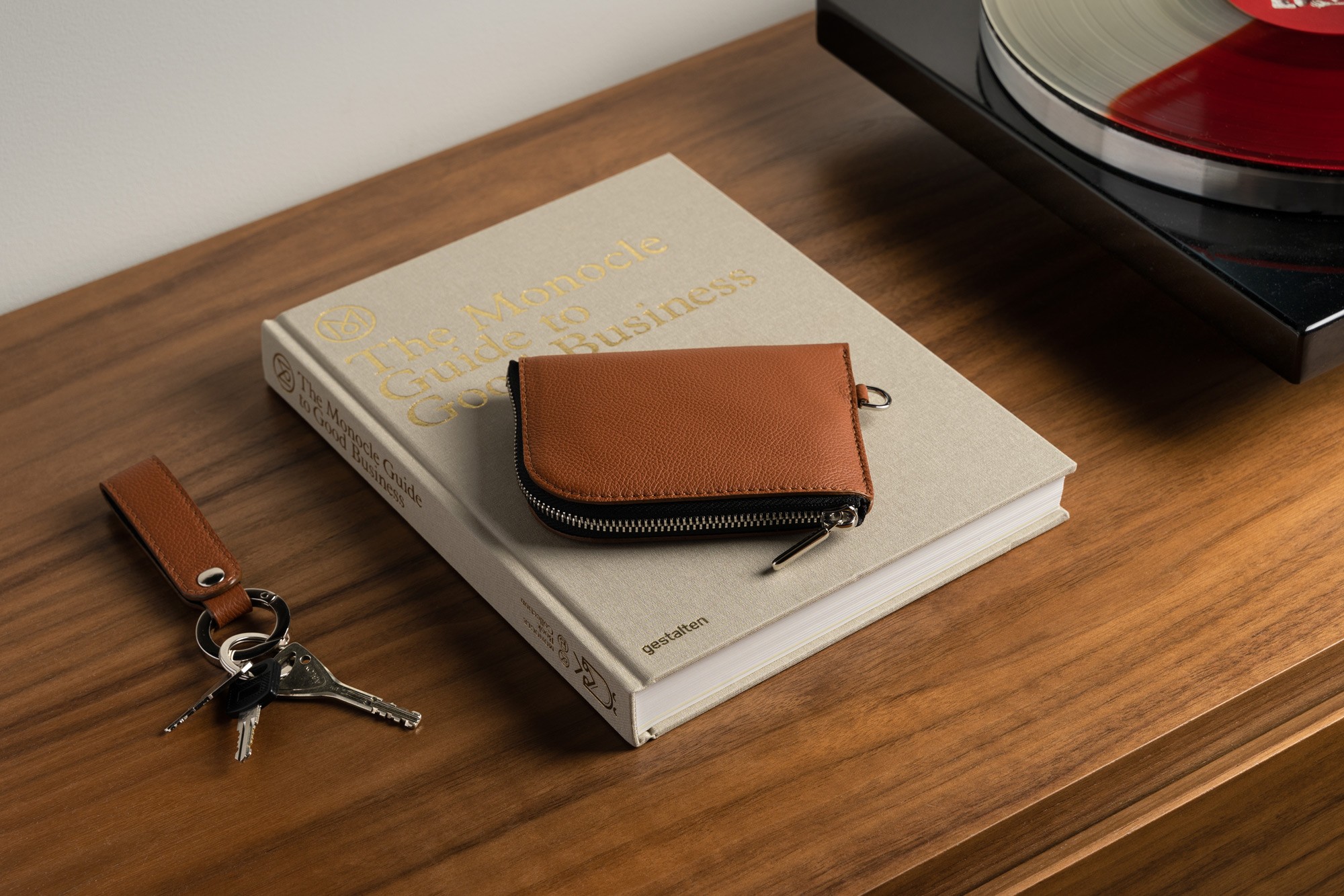 Photo of a leather zip wallet on a wooden table next to a vinyl record