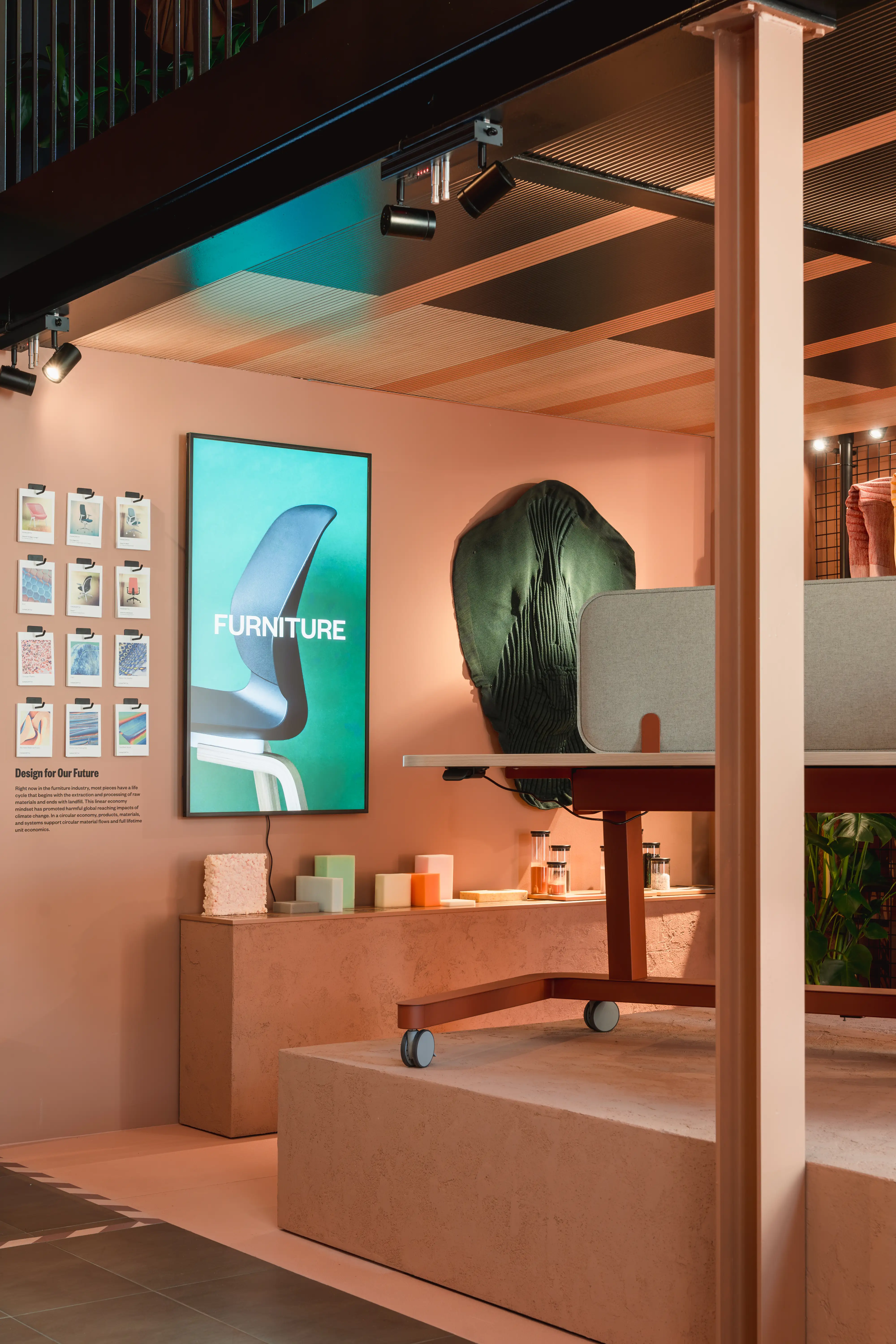 Furniture display with screen, height-adjustable desk and material samples in the peach-colored Haworth showroom.