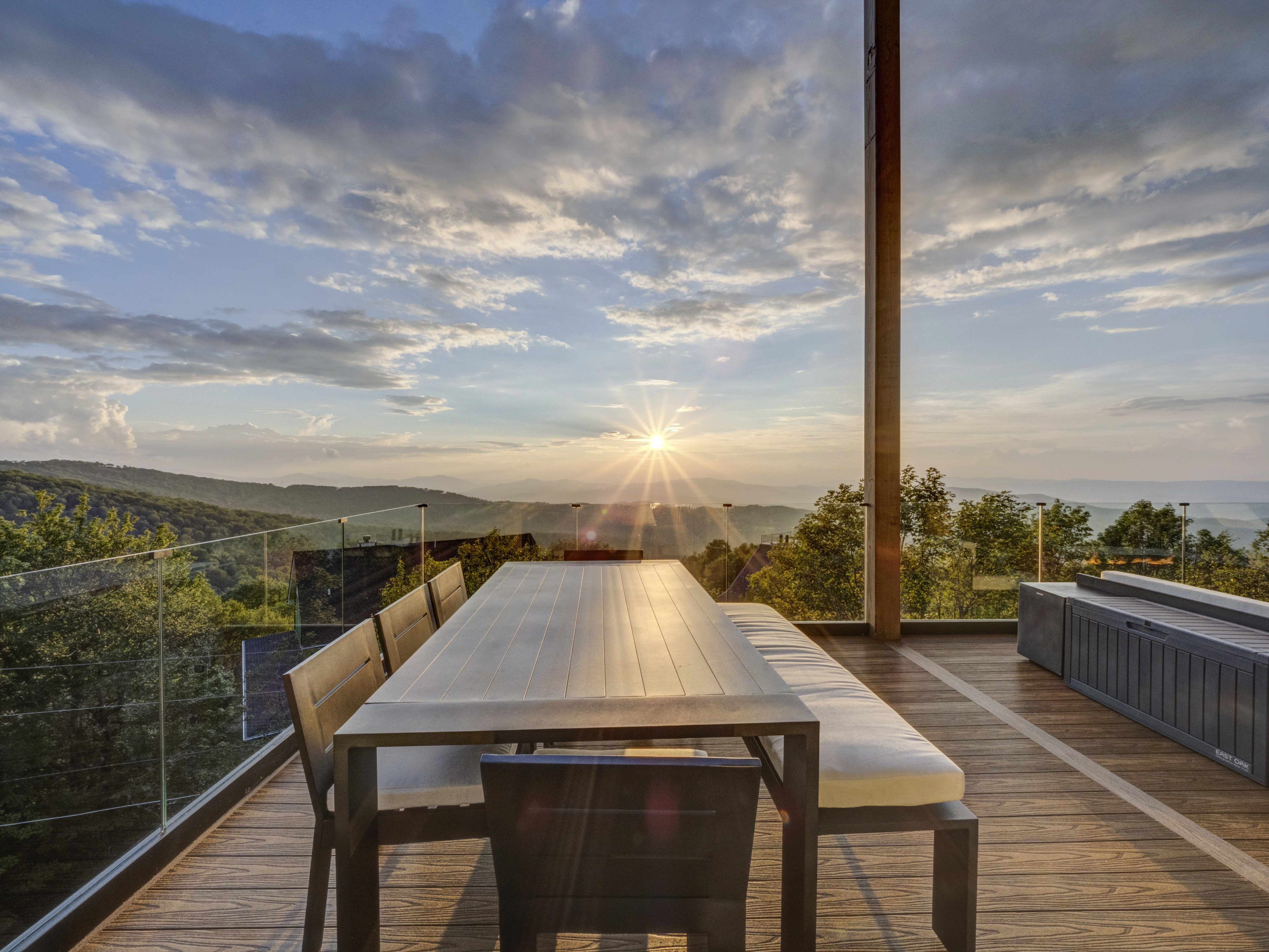 Minimalist outdoor dining table and bench on a covered wooden porch with an expansive view of rolling hills