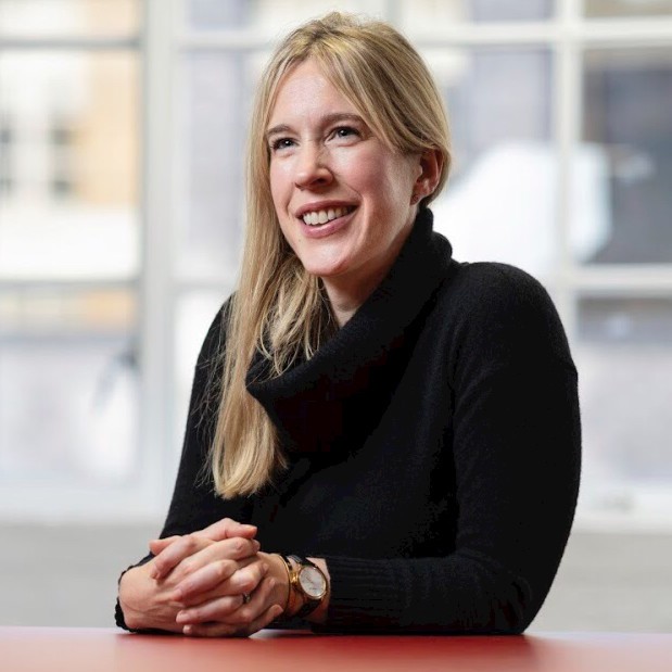 A young man with dark hair smiles at the camera, set against a modern indoor background.