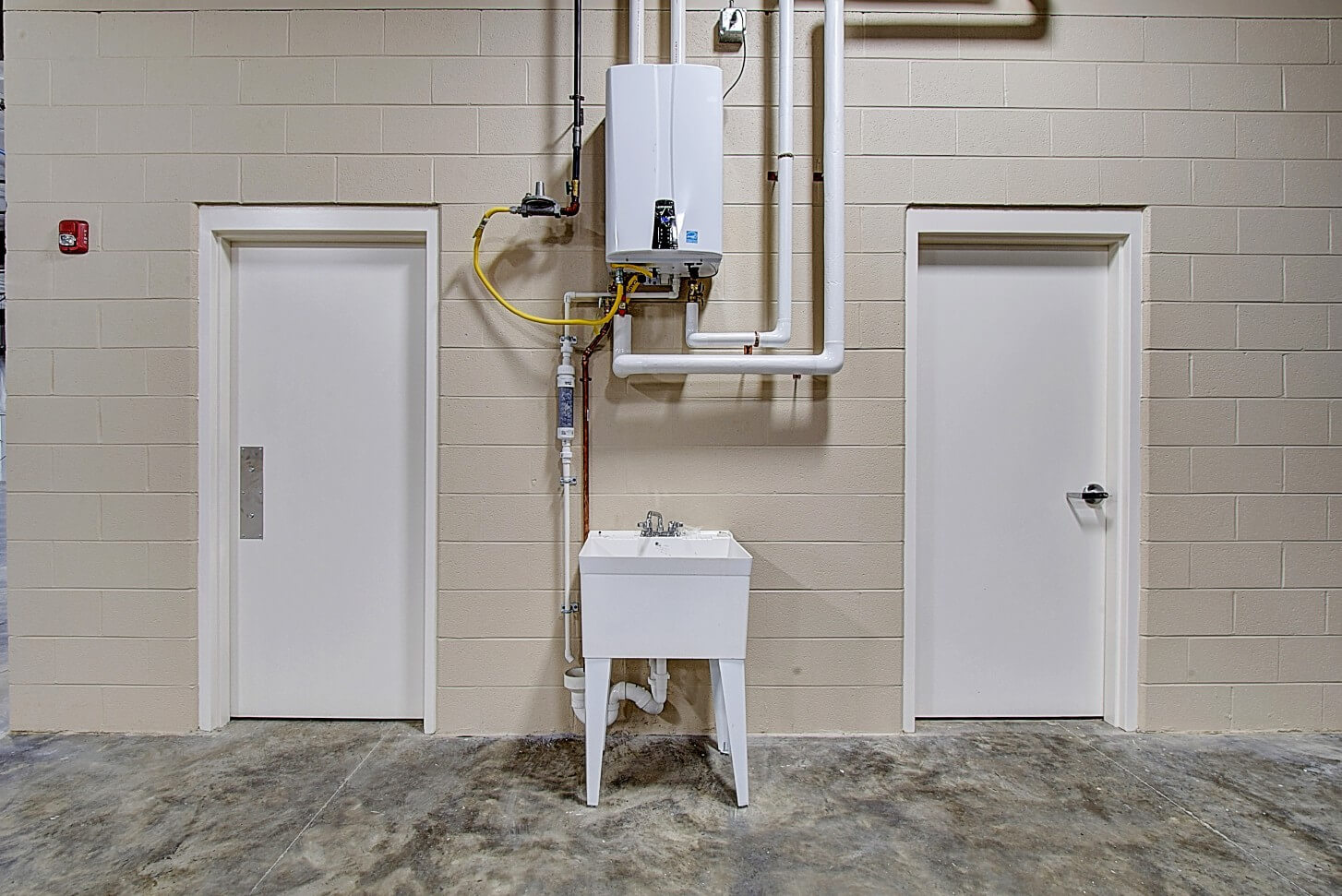 Two closed doors on either side of a small white sink against a plain wall.