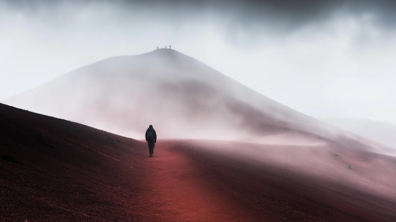A person walks along a red path shrouded in fog, creating a mysterious and serene atmosphere.
