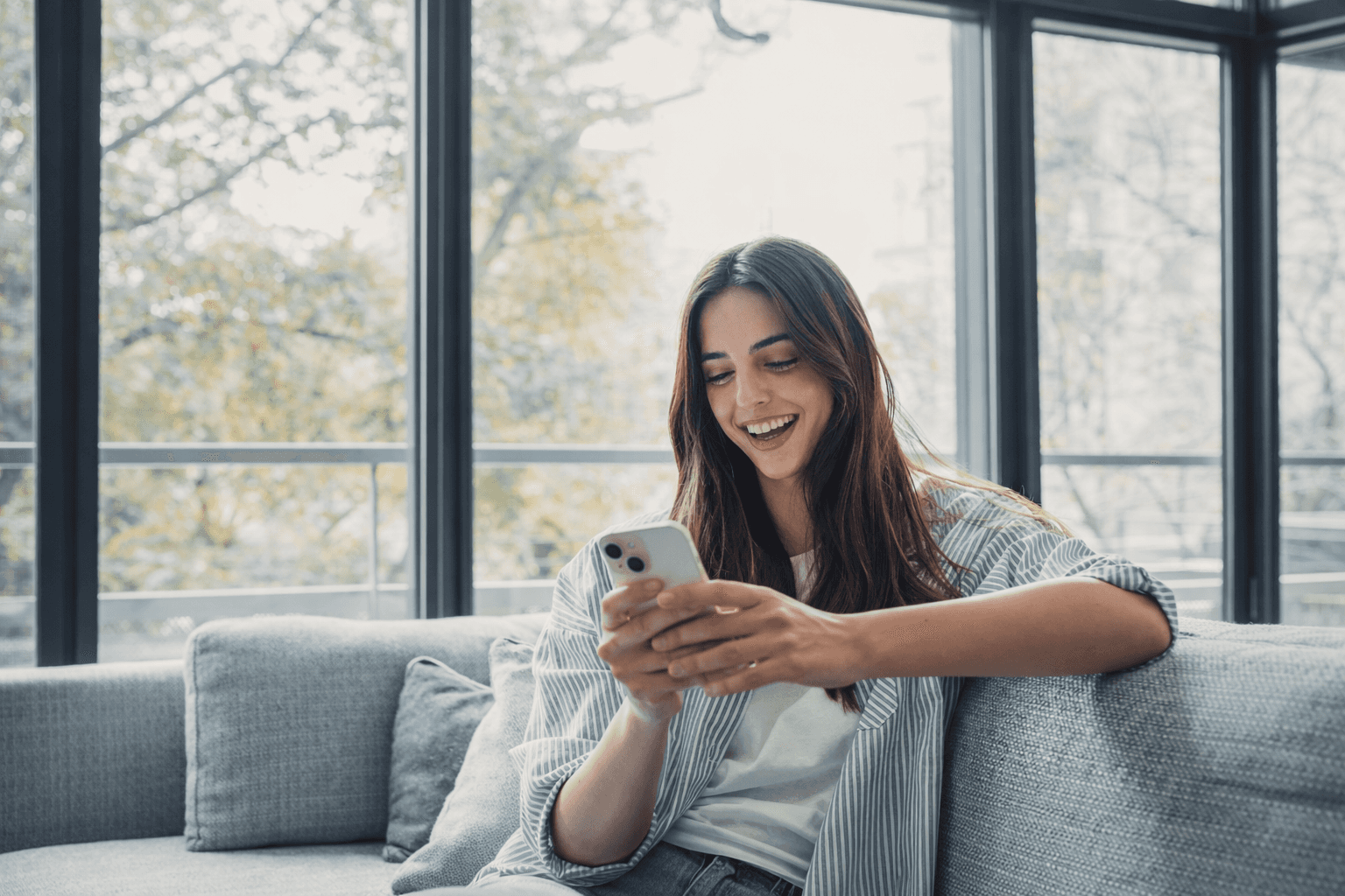 Man wearing headphones and a white t-shirt working on a laptop in soft natural light, with window shadows cast on the wall.