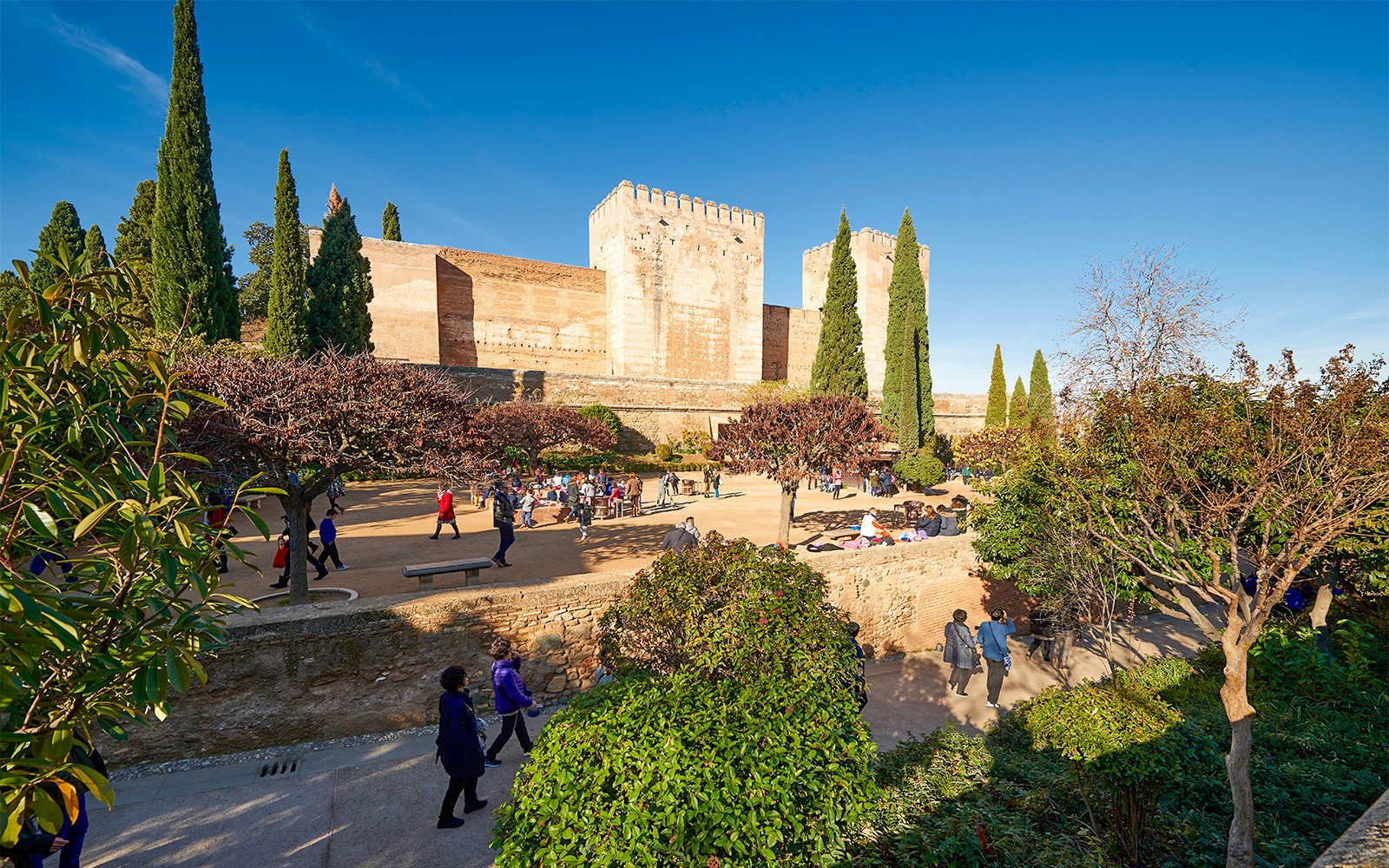 Visitors exploring Alhambra gardens with fortress walls in Granada, Spain.