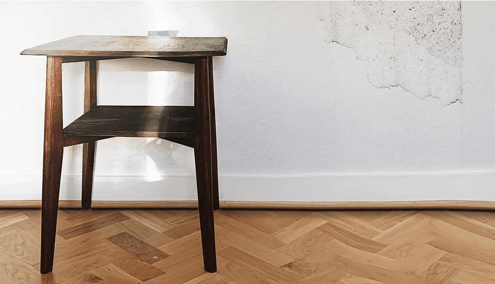 Interior wall with visible moisture damage and peeling paint near a wooden side table.