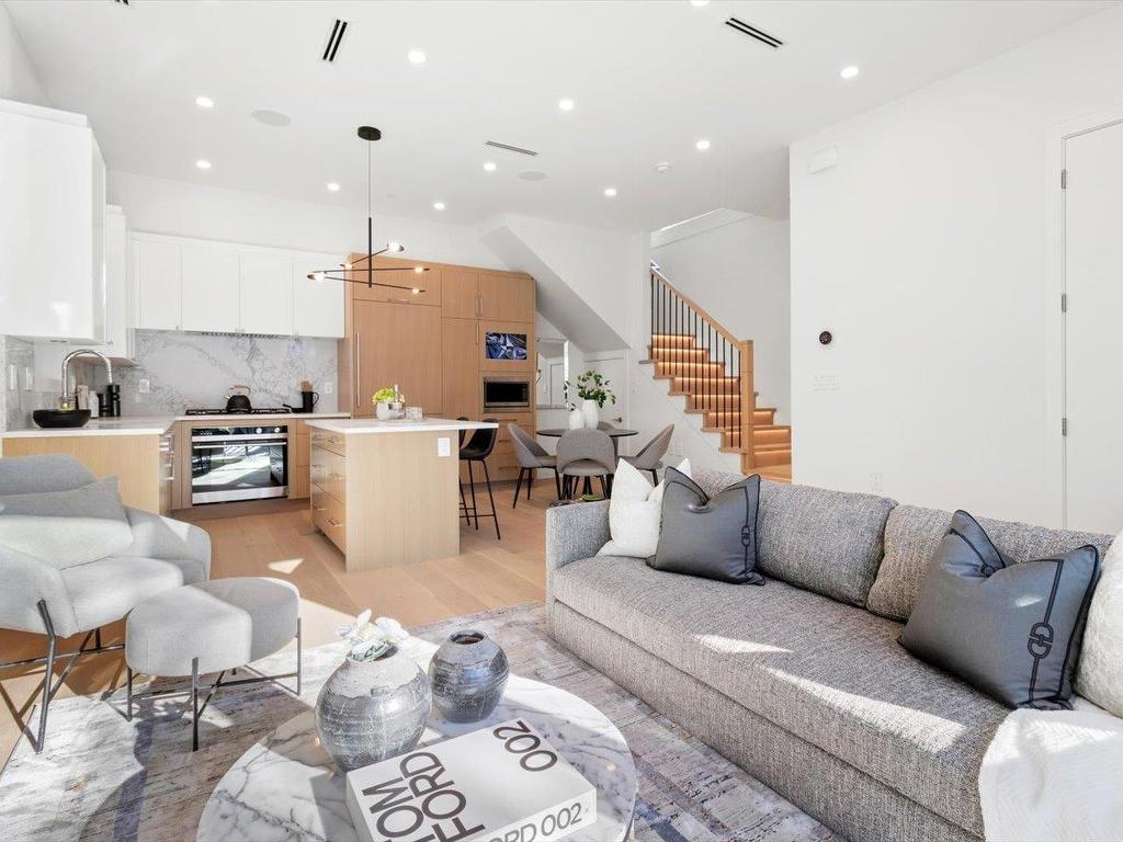 Modern open-concept living space with a gray sofa, light wood accents, and a staircase leading to the upper level.