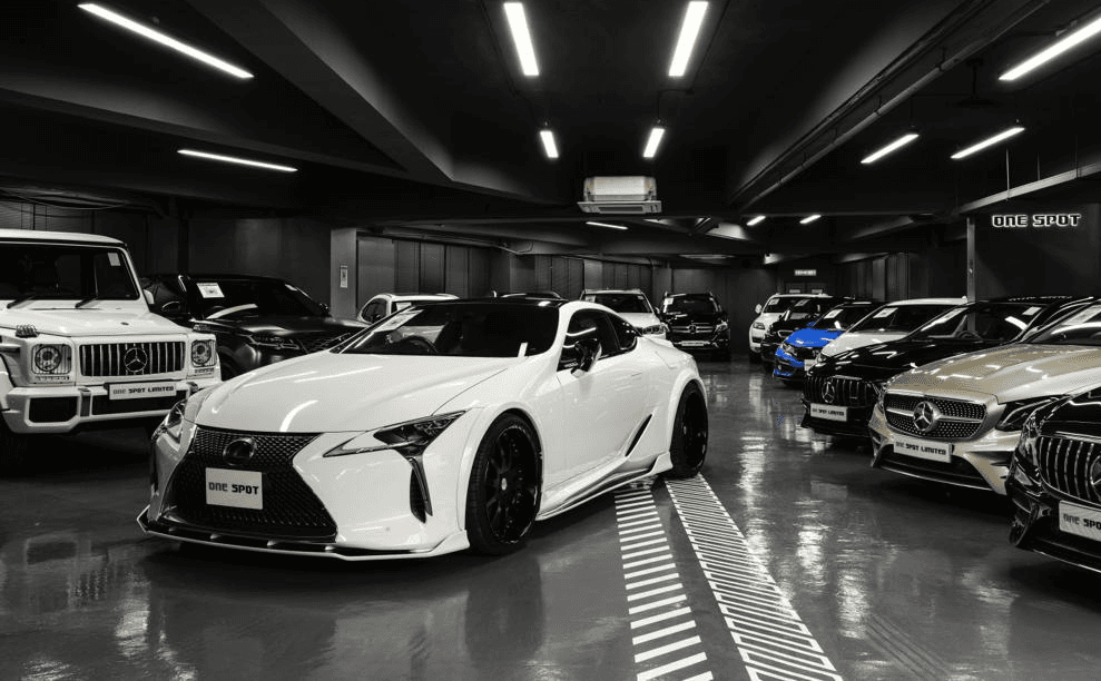 A white 2017 Lexus LC500 in the centre of a dark colour themed car showroom with different brands of cars in the background.