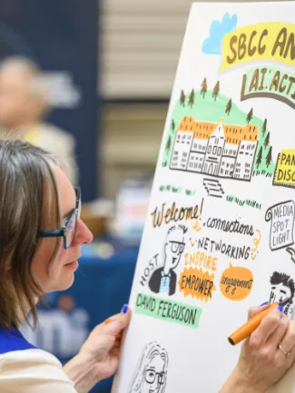 A woman sketches on a large poster featuring a building, trees, and words like "Welcome," "Inspire," and "Empower" at a networking event.