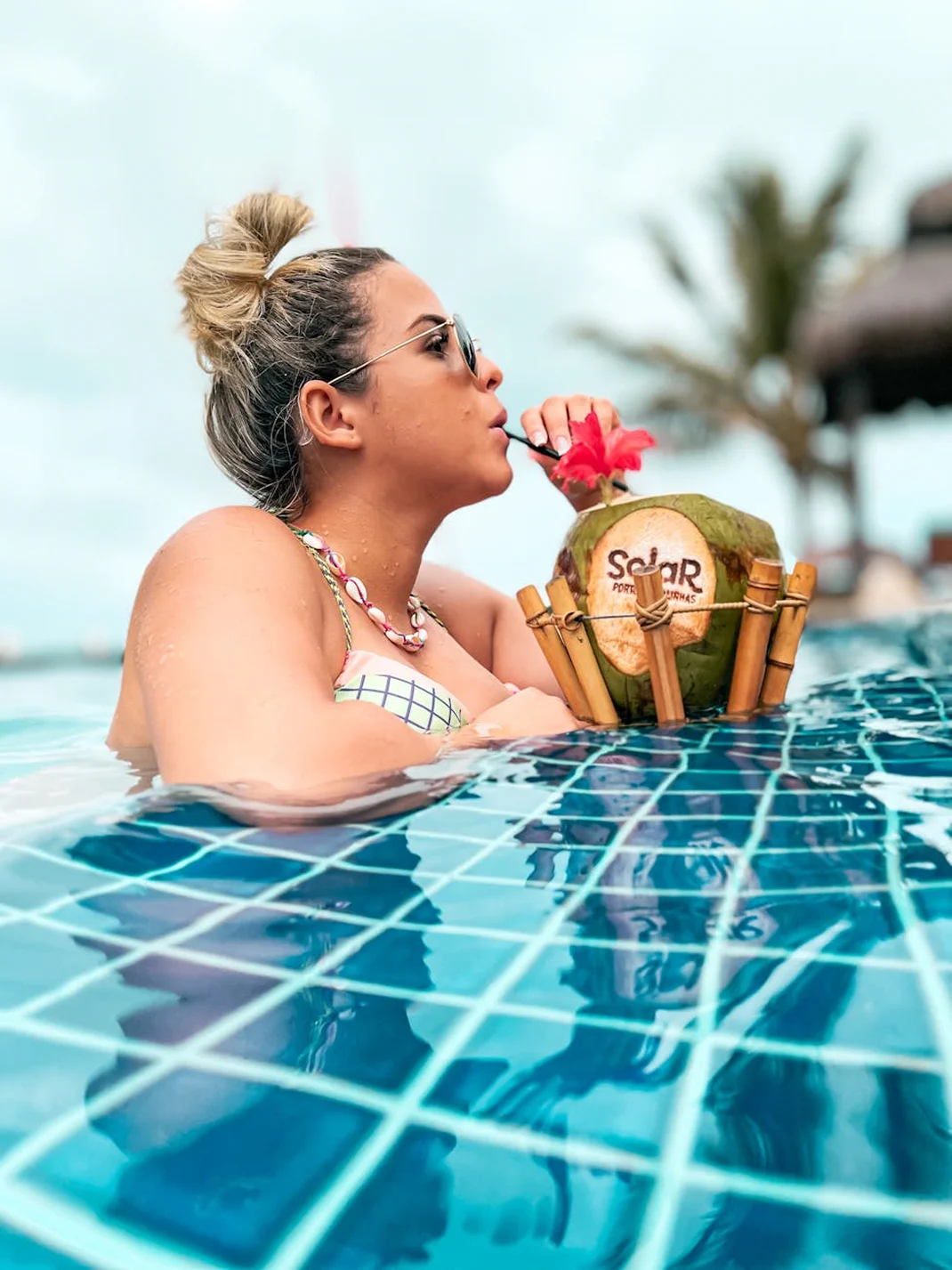 Guest relaxing in a swimming pool while drinking from a fresh coconut.
