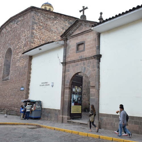 人們走過一個拱形入口，旁邊有一個歷史悠久的石頭建築，上面有一個十字架，還有一位街頭小販。