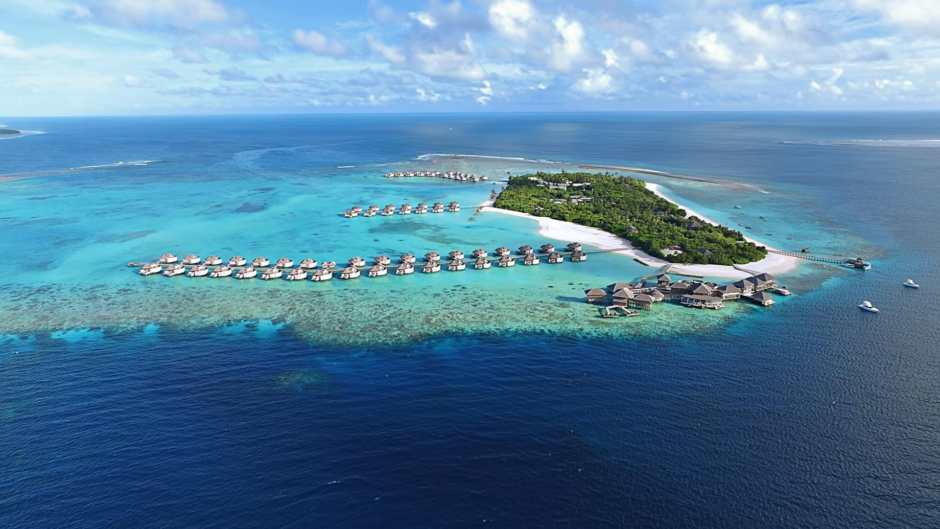 Aerial view of a Maldives island resort featuring overwater villas, tropical greenery, and vibrant blue lagoons.