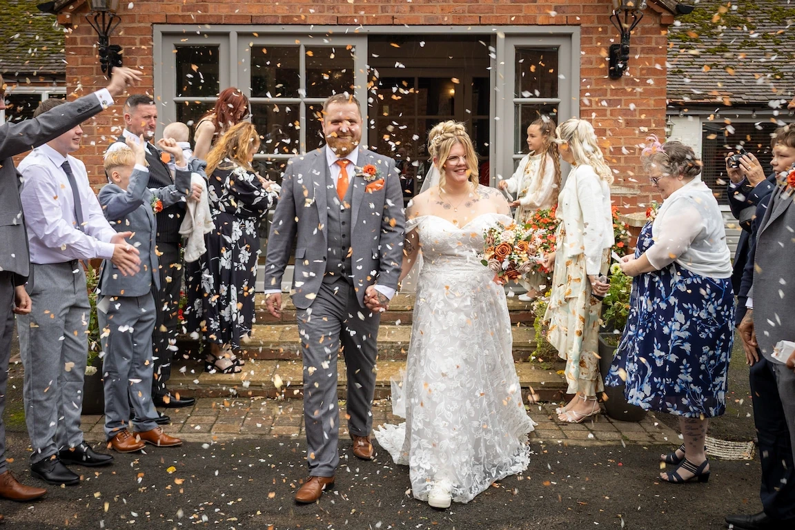 Hannah and Shawn walking through confetti outside the Charlecote Pheasant Hotel after their ceremony