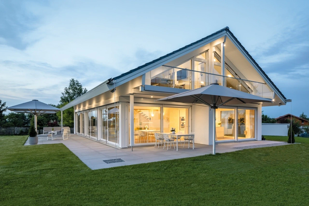Modern house with large windows, patio, and umbrellas at dusk.