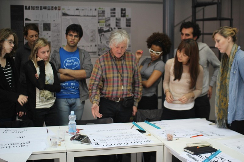 A photo of a teacher talking to the students while they draw different typographical letters.