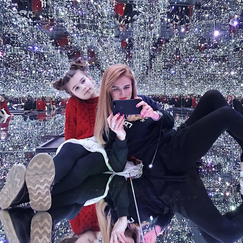 两个人在一个充满小灯光的镜面房间中拍照,创造出闪烁的无限反射效果。