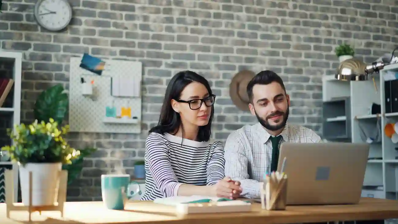 Two business professionals working together on a laptop in an office, representing sponsorship relationship management, sponsor updates and renewal strategy for sports clubs.