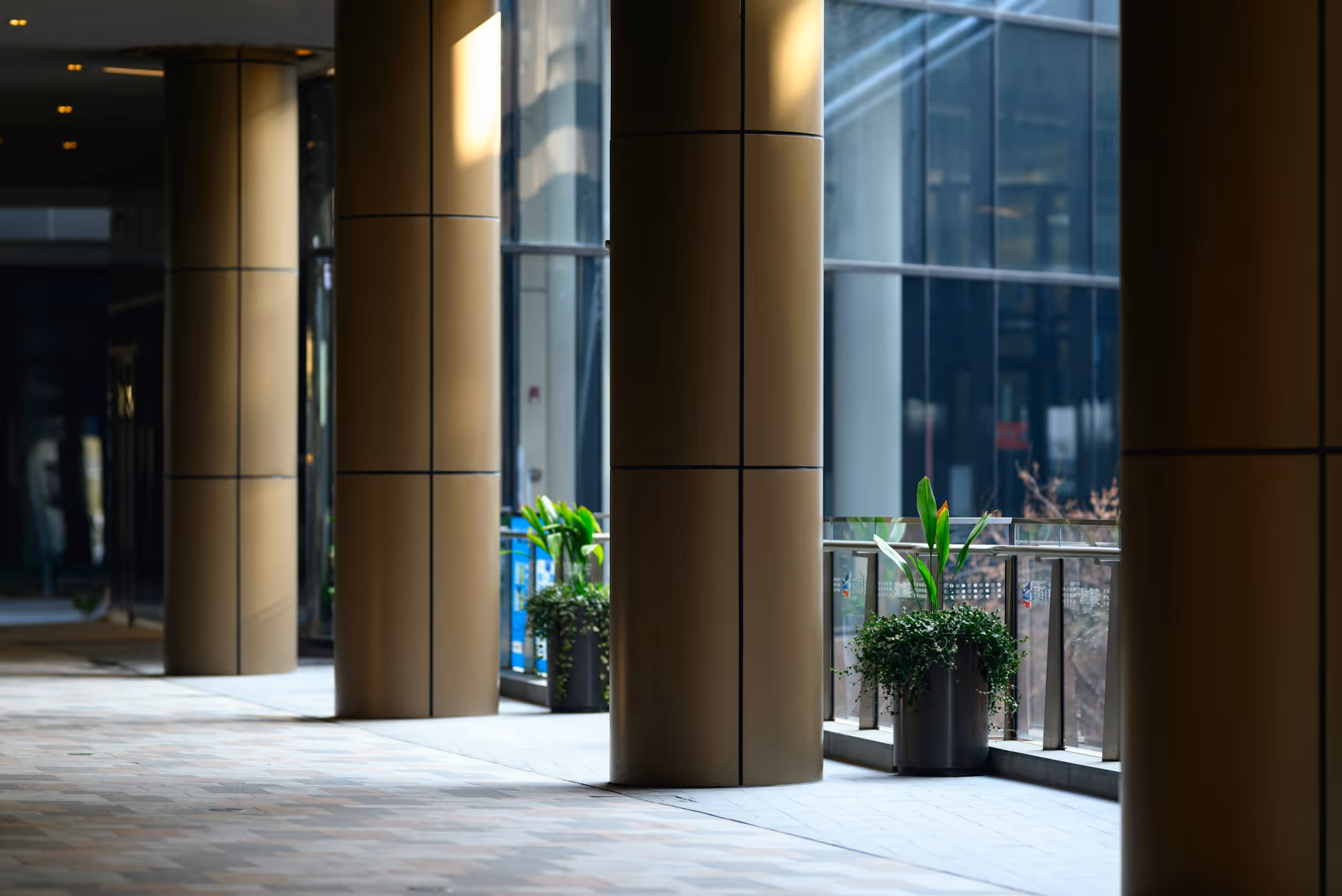 Polished bronze columns lining a modern building lobby, with glass walls and potted plants in the background.