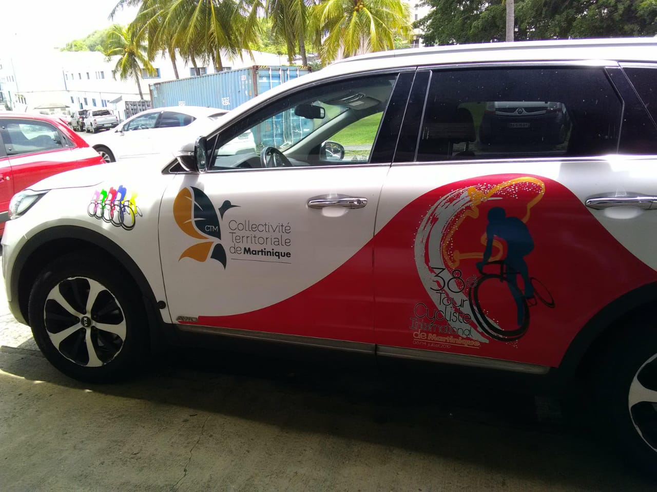Voiture blanche avec des autocollants colorés pour le 38e Tour Cycliste International de Martinique. Les graphismes représentent des cyclistes colorés et des palmiers en arrière-plan.