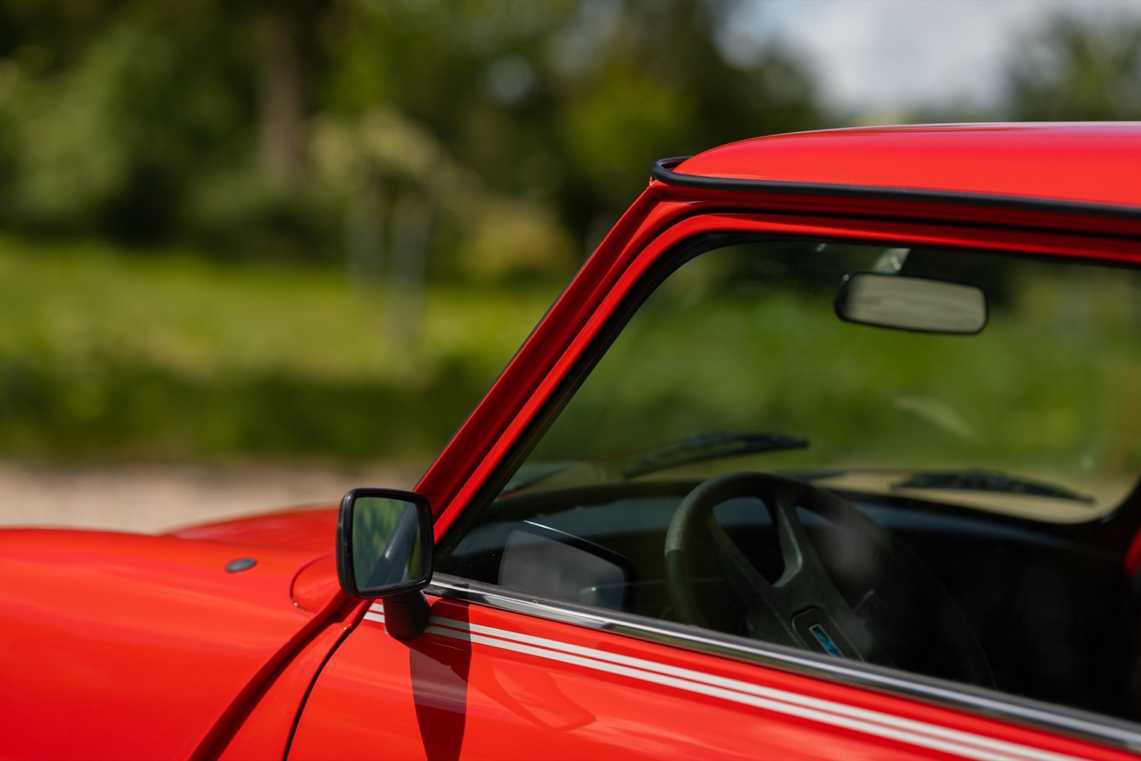 Close-up of a red car's side window and frame, with a blurred green background.