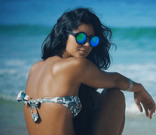 Editorial fashion film frame of a woman looking at the camera with sunglasses wearing a bikini at the beach