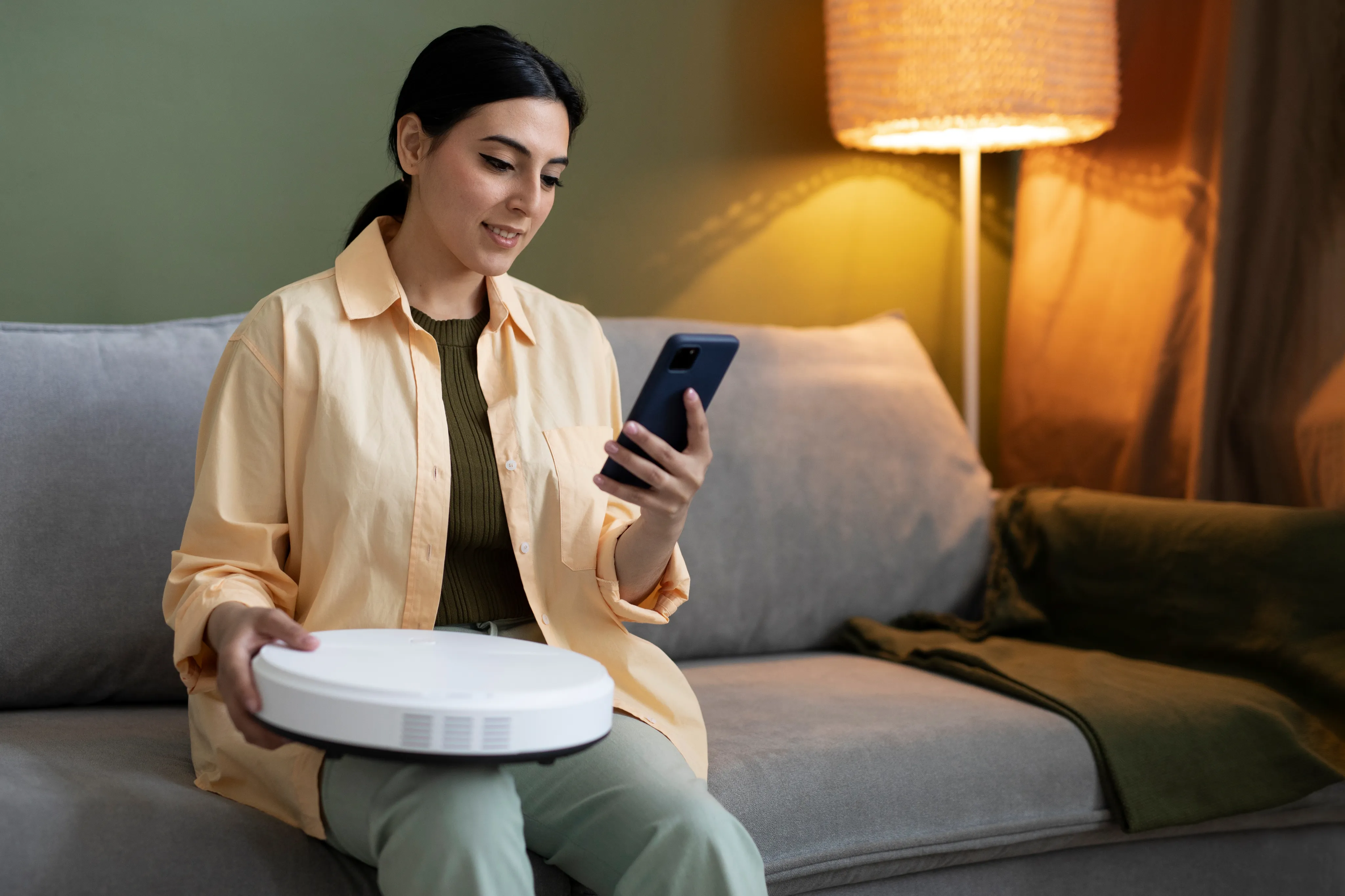 Woman sitting on a living room sofa using a smartphone for smart home post-install support.