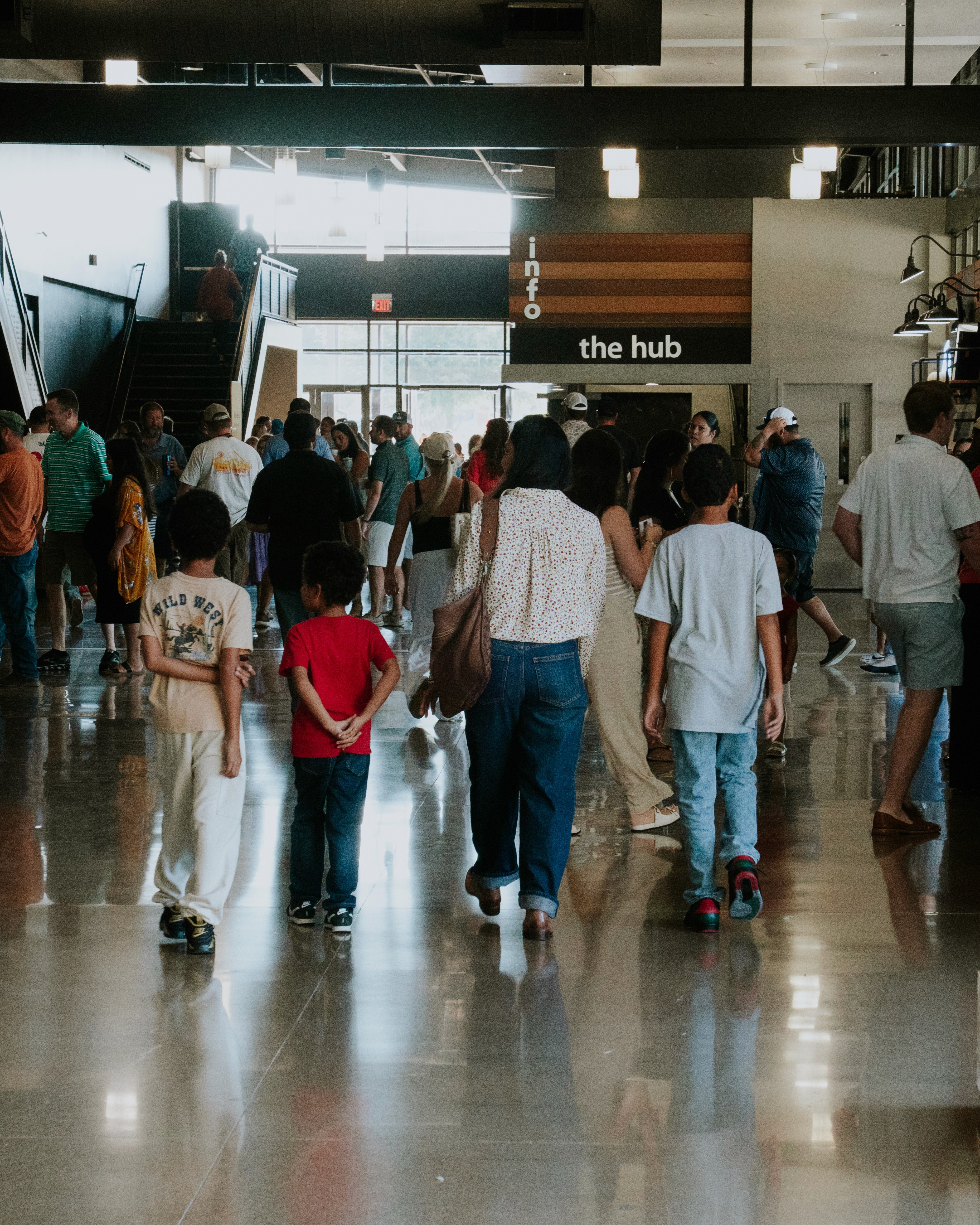 Children playing in a splash pad, laughing and enjoying water on a sunny day, with trees and cars in the background.
