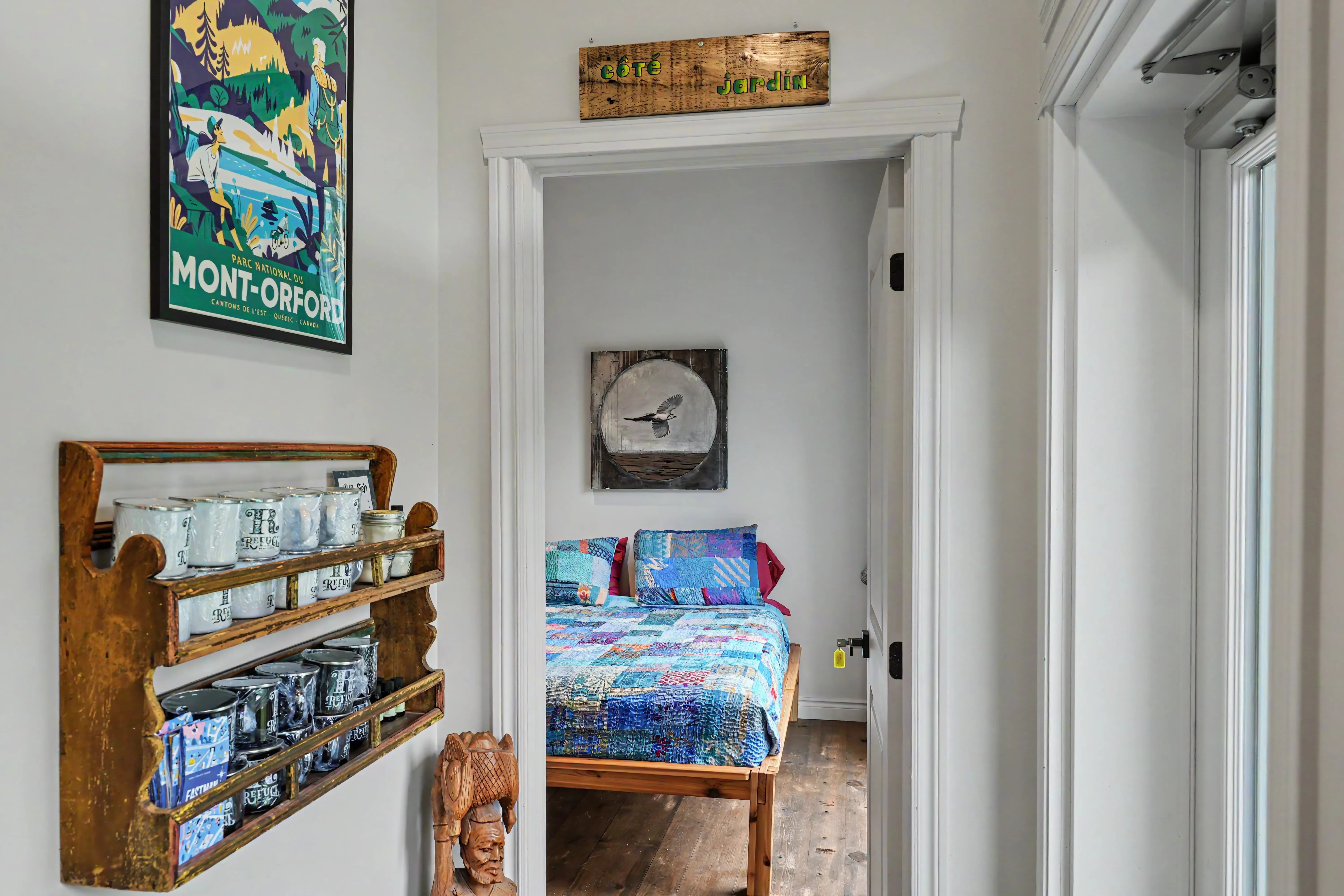 Chambre du gîte R112-Nord avec lit double recouvert d’une courtepointe patchwork bleue et verte, étagère murale en bois et affiche vintage du parc national du Mont-Orford.