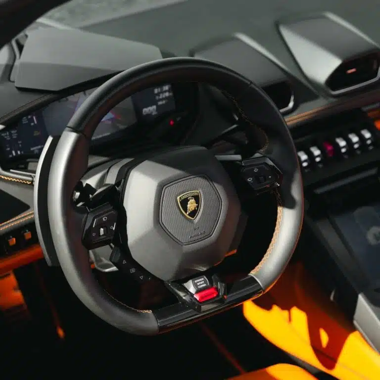  Interior shot of the Lamborghini Huracán EVO Spyder's steering wheel and digital dashboard, featuring vibrant orange and black accents.