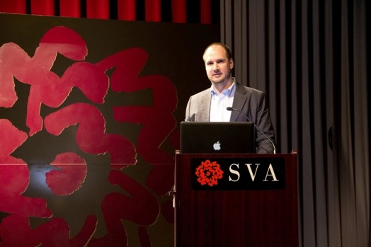 a man giving a speech from a stand in the "designer as" thesis presentation