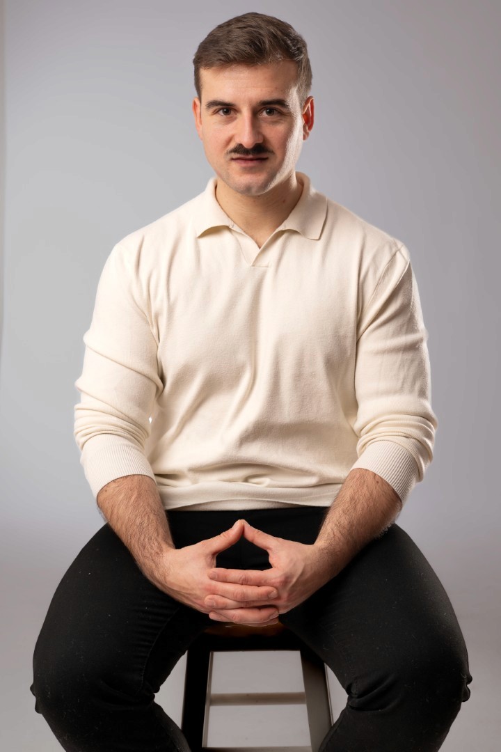A man sitting on a stool having his portrait taken.