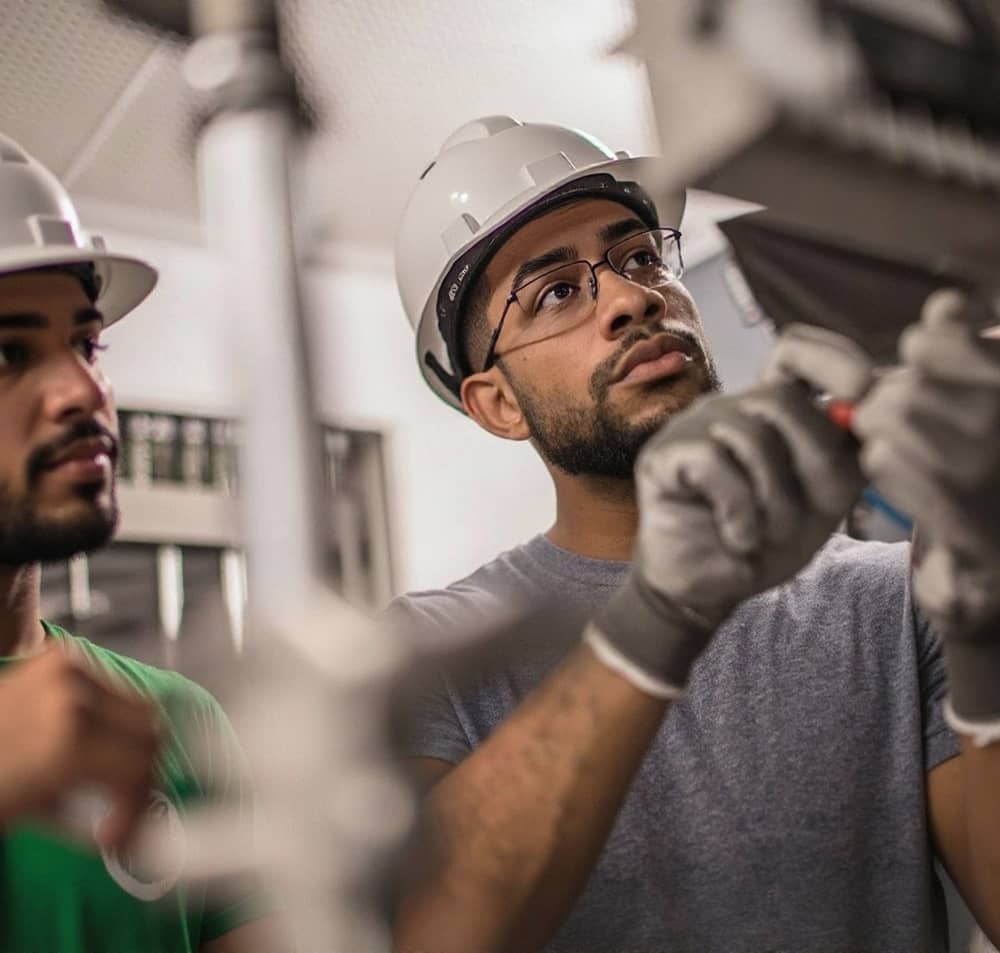Deux électriciens portant des casques de sécurité travaillent sur une installation électrique.