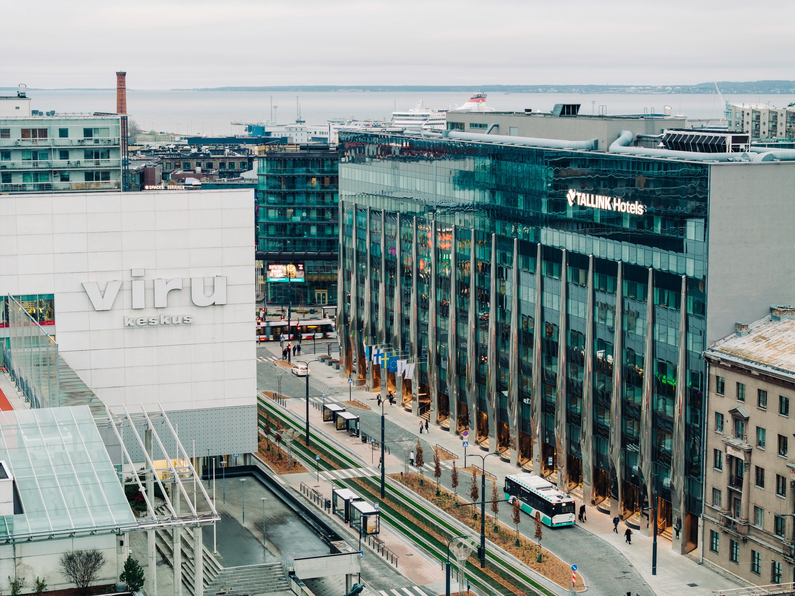 Elevated diagonal view across Viru Keskus toward the Tallink Hotels facade and tram corridor, with the waterfront and city layers behind.