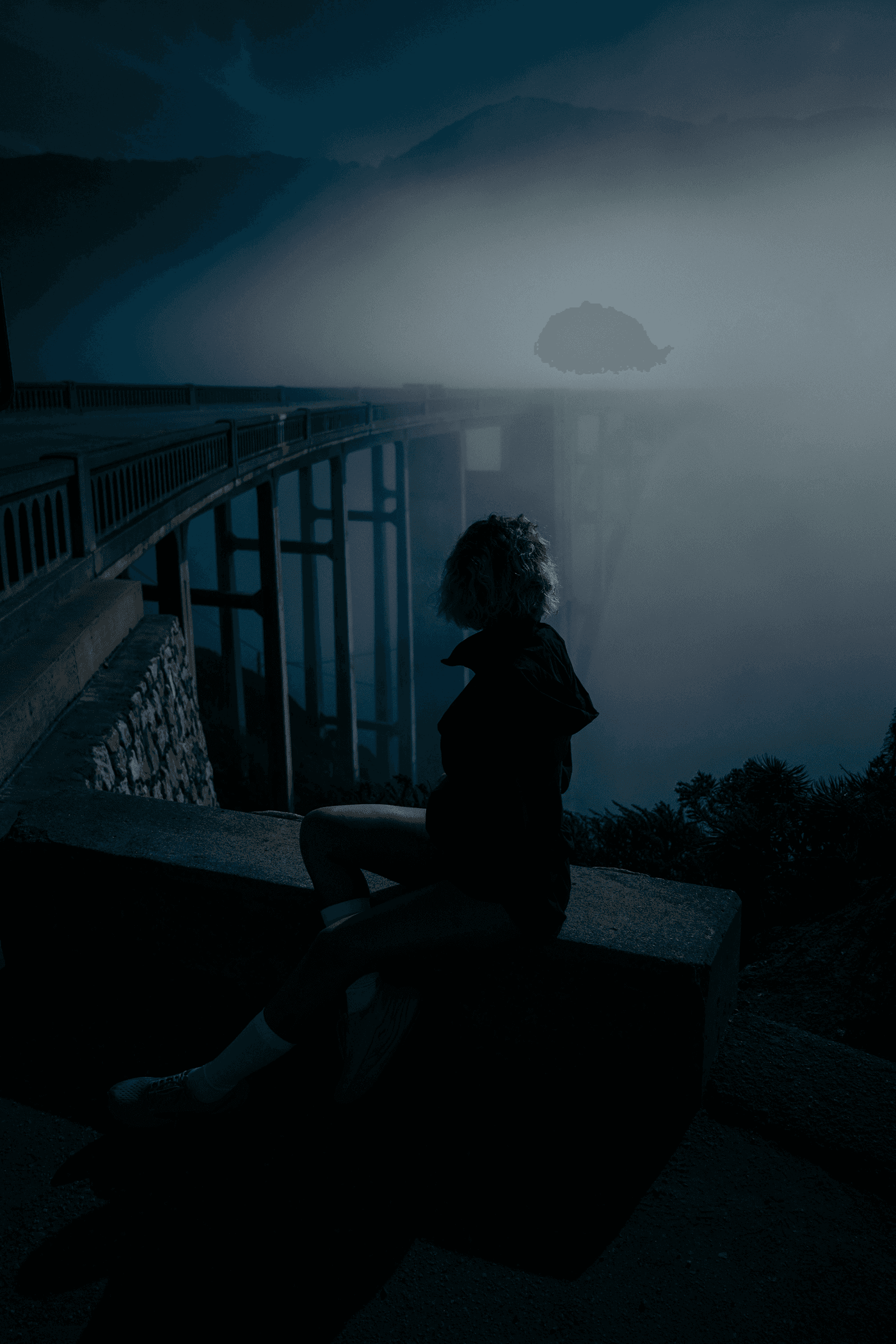 Person sitting beside dark bridge.