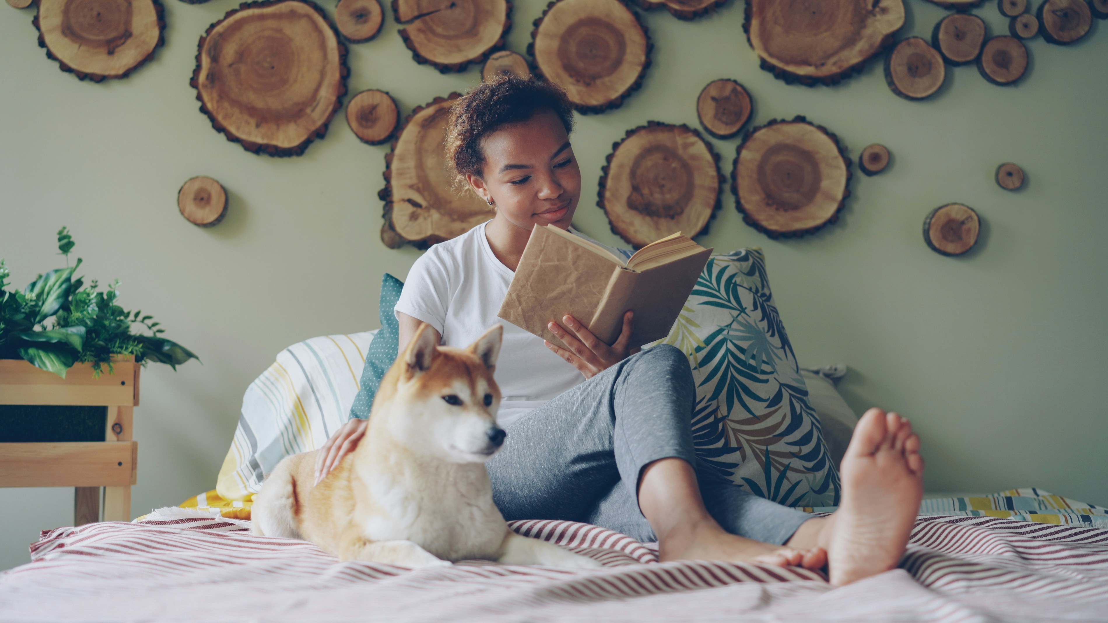 A girl reads with her dog on the bed.