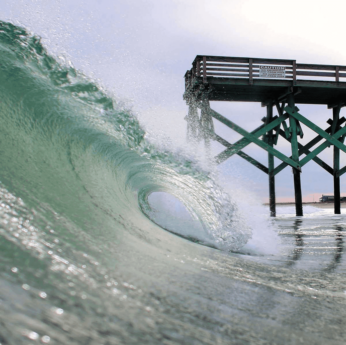 Large wave crashing under pier – surfboard rental in wrightsville-beach