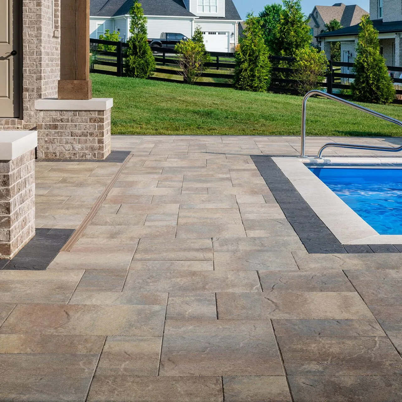 Warm rectangular pavers with a dark border beside a swimming pool and covered terrace.