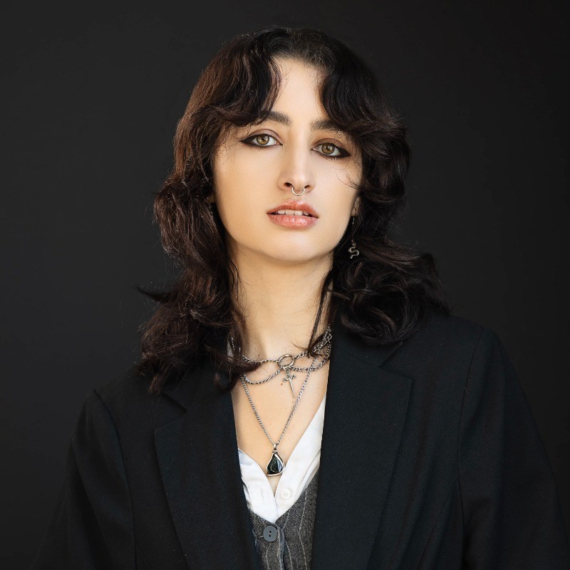 A thoughtful young person with dark hair gazes to the side, captured in soft black and white lighting.