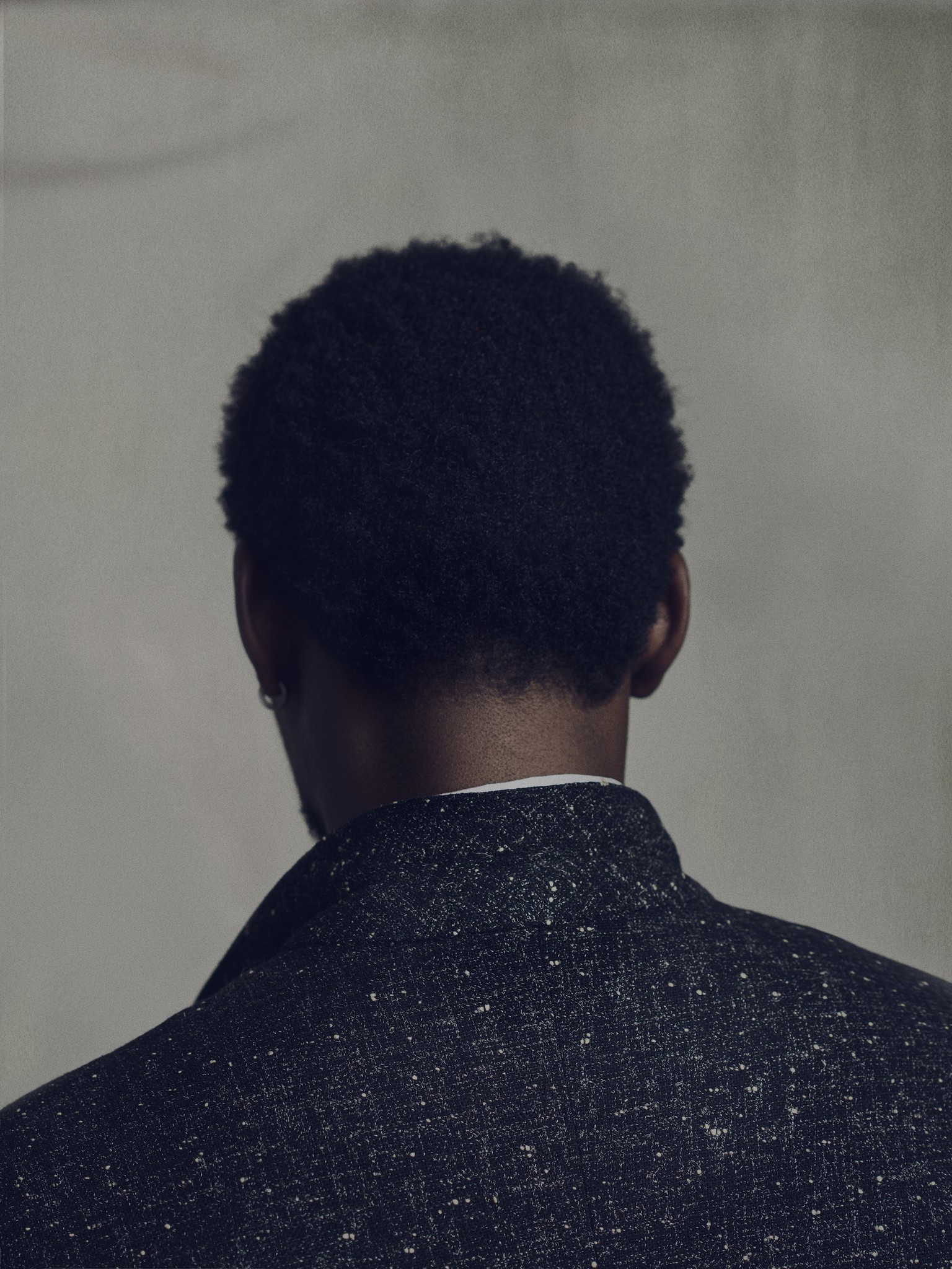 A photographic portrait of a black man. the subject is turned away from the viewer. 