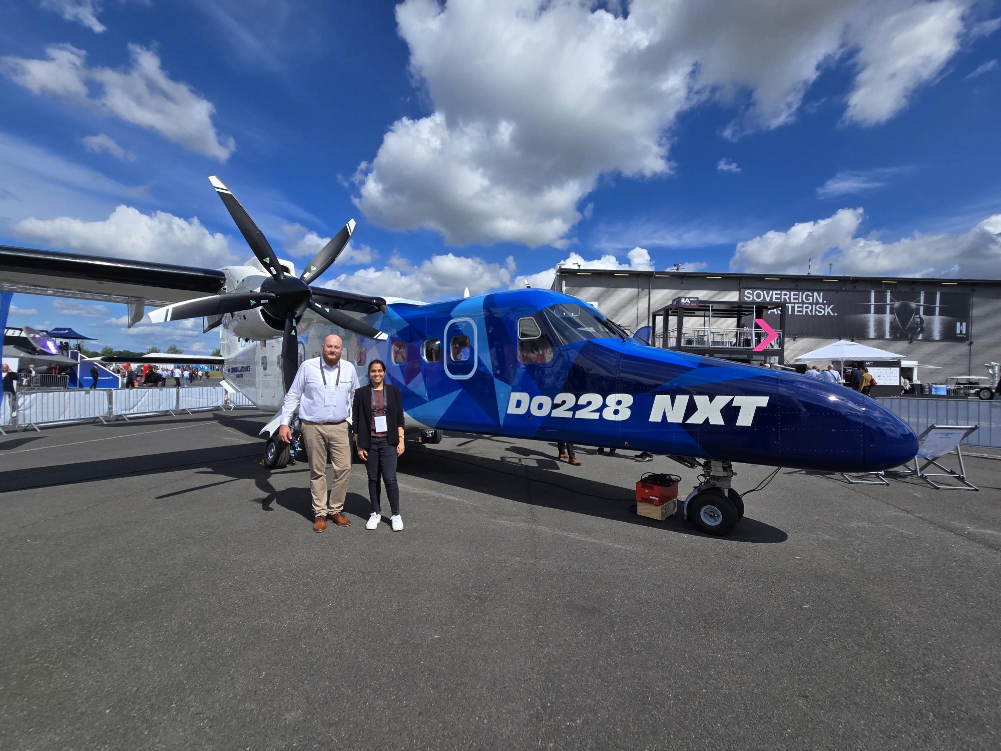 Woman and Man standing in front of an airplane with the Name Do228 NXT. They're looking in the camera