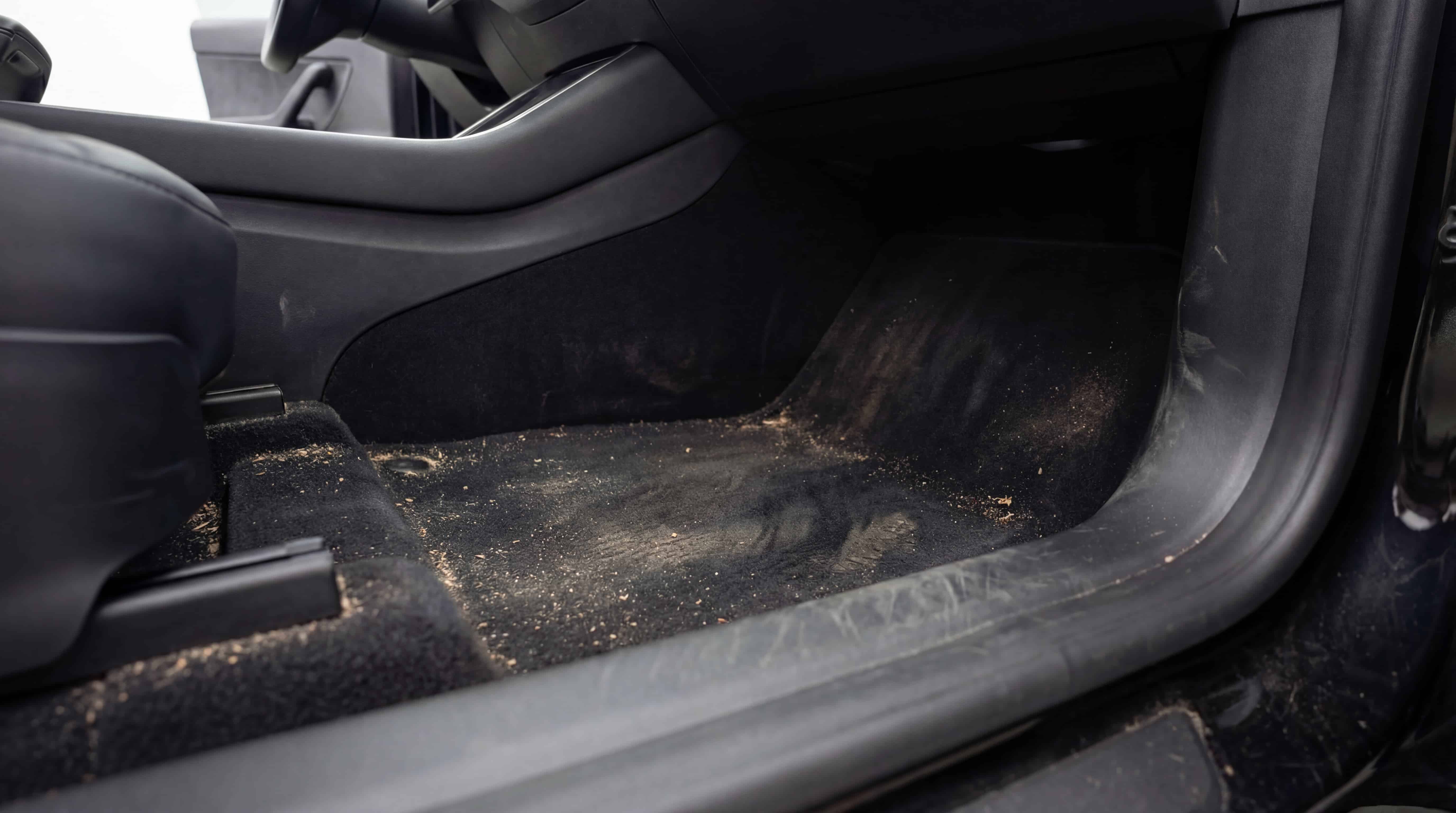 Avant nettoyage des moquettes intérieures d’une Tesla Model Y avec poussières et résidus