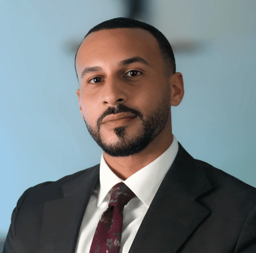 A woman with short curly hair wearing a black t-shirt looks into the camera.