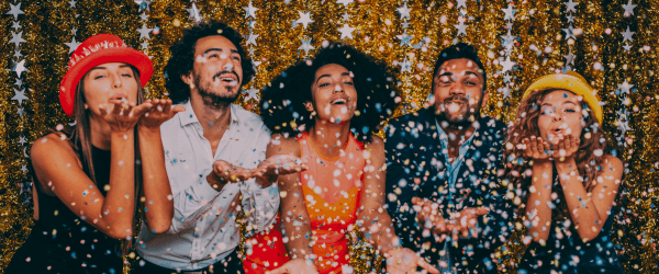 A group of firiends blowing confetti in front of a gold backdrop