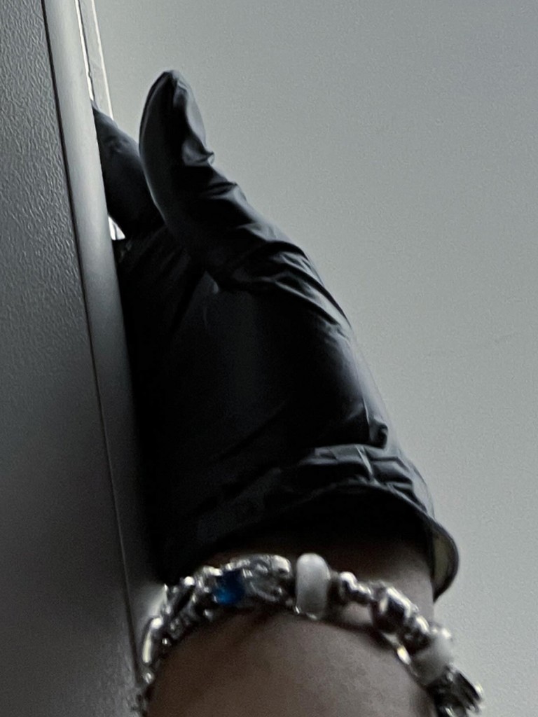 "Hand wearing a black nitrile glove with a bracelet"