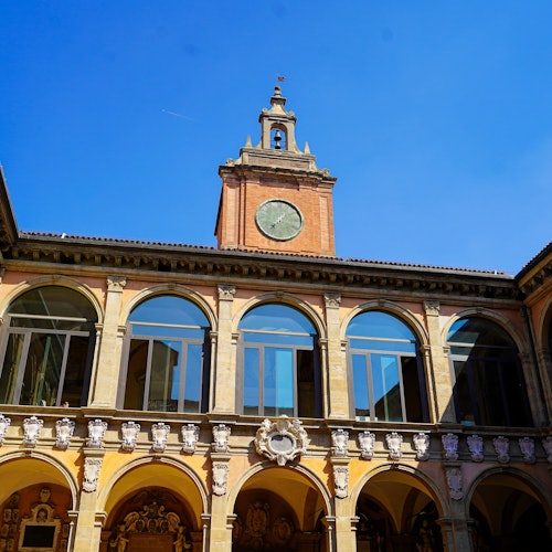 מבנה היסטורי עם חלונות מקושתים, מגדל שעון ופרטי אדריכלות מורכבים, תחת שמיים כחולים וצלולים.