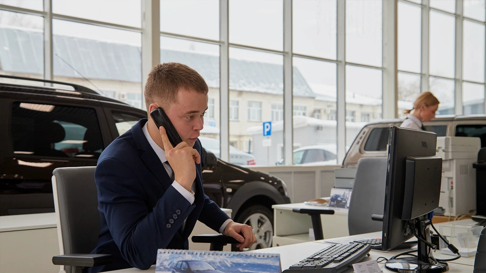 Kirov, Russia - February 26: Handsome male Manager in a suit with phone in showroom of dealership Autovaz and car Lada in Kirov city in 2019